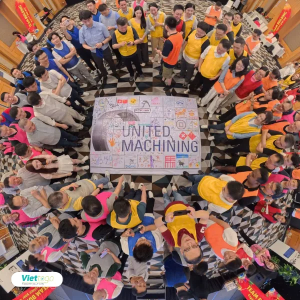 Team building indoor United Machining — nhóm nhân viên xếp vòng tròn quanh bức vẽ tập thể